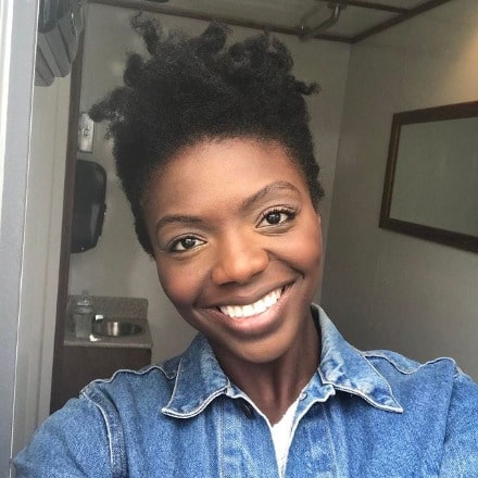 Sasha Morfaw posing by wearing blue jeans and white vest.